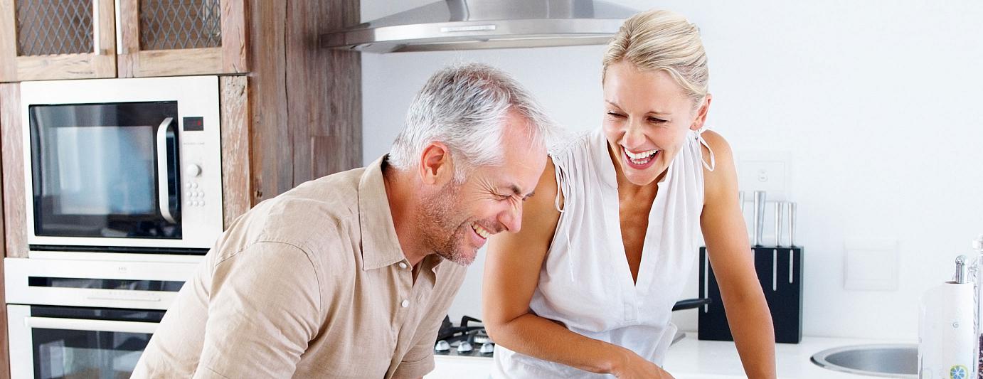 IDEAL Hausratversicherung: Frau und Mann lachen in der Küche beim Kochen